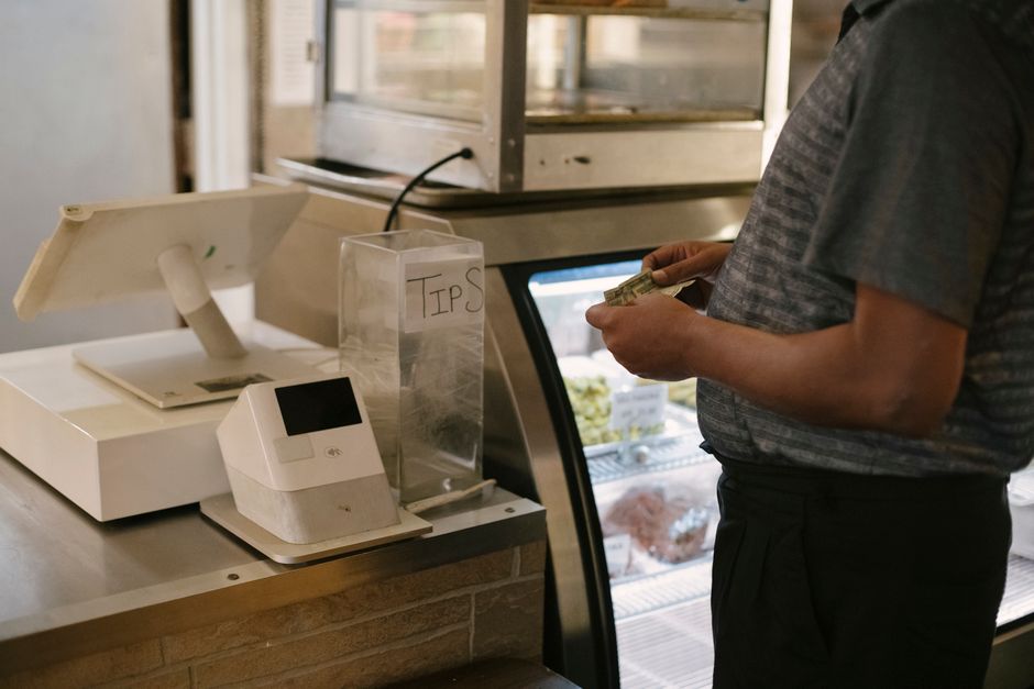 A customer in casual clothes stands at a cash register in a grocery store, preparing to make a purchase near a glass showcase.