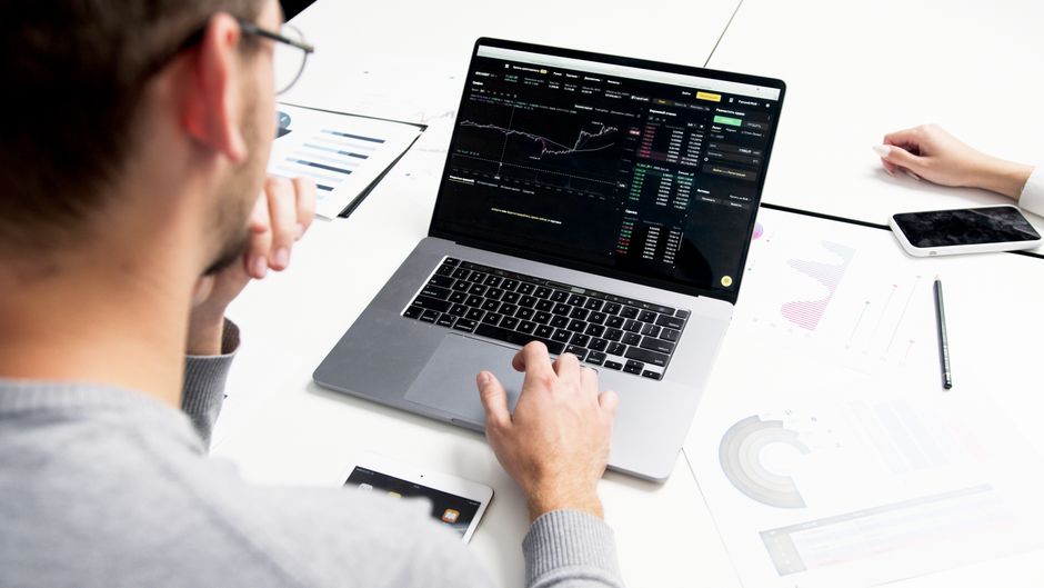 A market participant reviews price charts and financial data on a laptop.