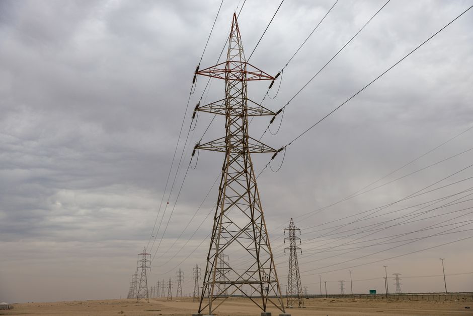 Power transmission towers stretch across a desert landscape under heavy clouds.