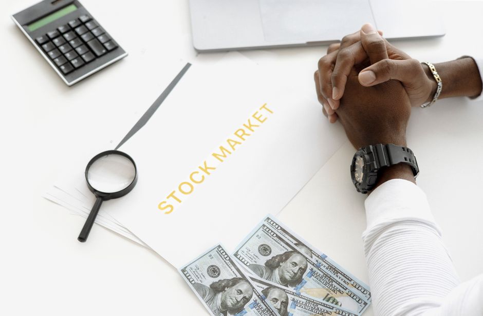 Hands resting over stock-market documents, a calculator and cash on a desk