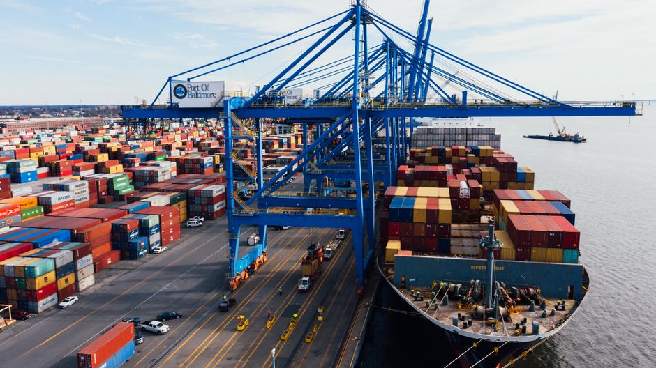 A cargo vessel loading containers at a port as shipping disruption raises fuel and freight risks for retailers.