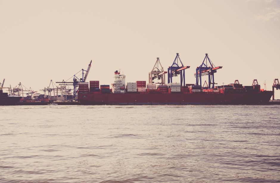 A cargo vessel and port cranes represent the export infrastructure exposed to maritime disruption.
