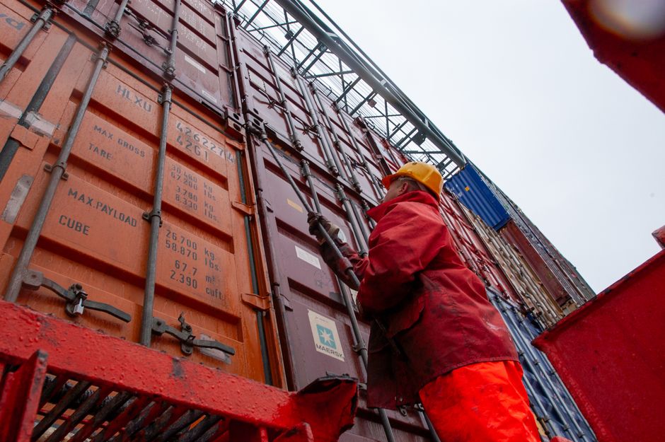 A worker secures cargo containers at a shipping port as imported goods move through the supply chain.