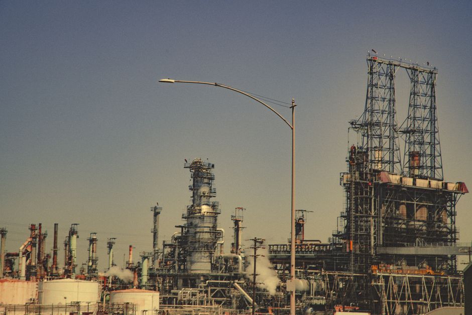 A large industrial oil refinery with pipes and towers under a clear blue sky, illustrating the energy infrastructure at risk from the Hormuz crisis.
