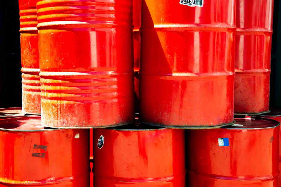 Stacked red industrial oil barrels outdoors in daylight.
