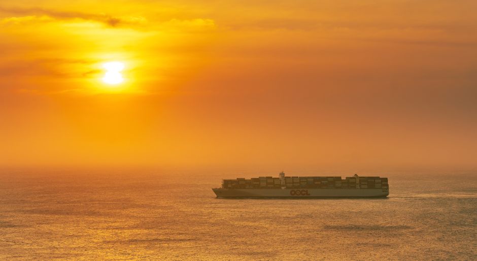 A large cargo container ship sailing across the ocean at sunset, illustrating global maritime trade routes.