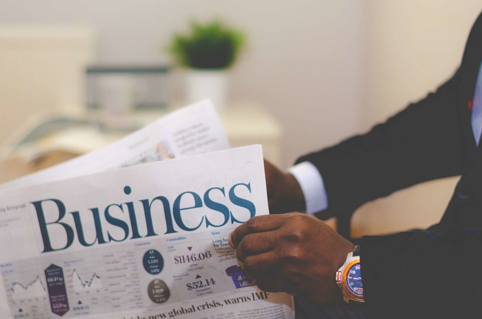 A person reading a business newspaper, focusing on financial headlines.
