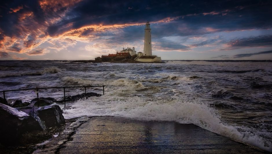 A lighthouse standing against a vibrant sunset over a stormy sea.