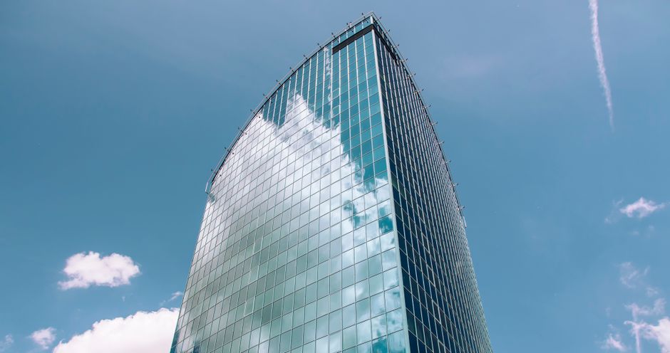 A sleek modern glass skyscraper with a reflective facade against a blue sky, symbolizing corporate technology infrastructure.