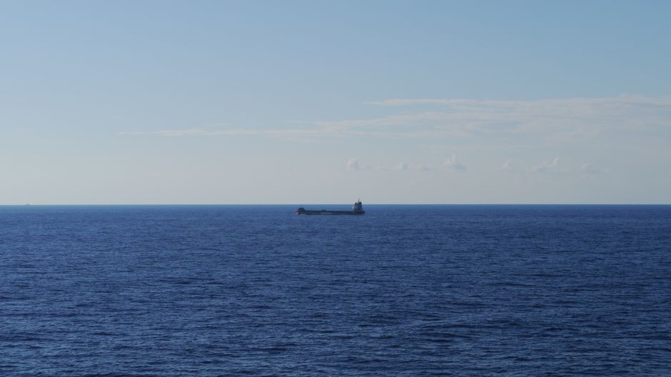 A bulk carrier ship cruising across the open ocean, illustrating the vulnerability of global maritime trade routes to geopolitical disruption.