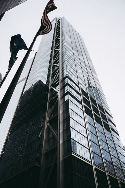 Low angle view of a modern skyscraper with reflective glass panels and flags.