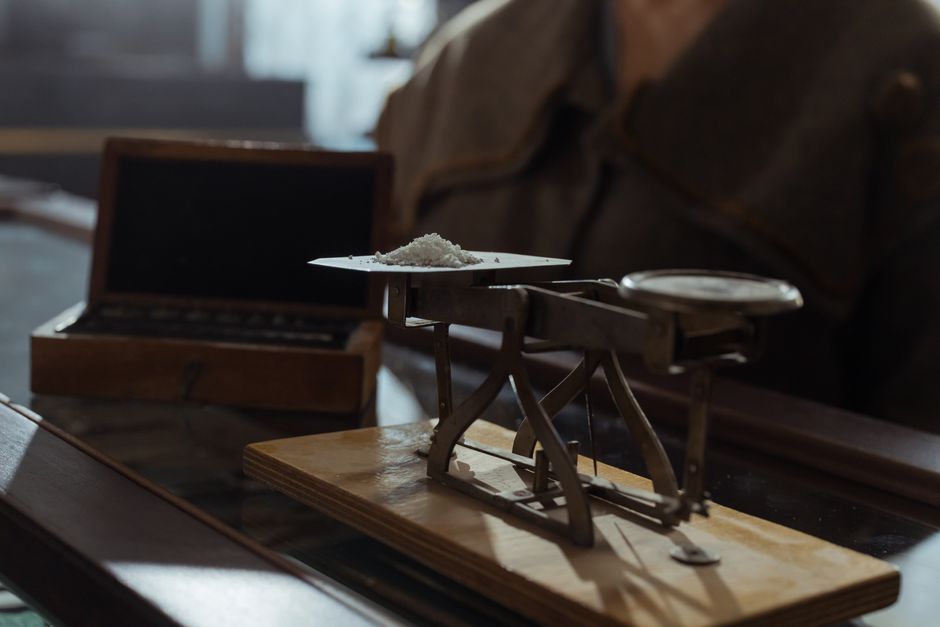 A vintage weighing scale with a small heap of white powder on a wooden surface, symbolizing the market weighing competing forces.