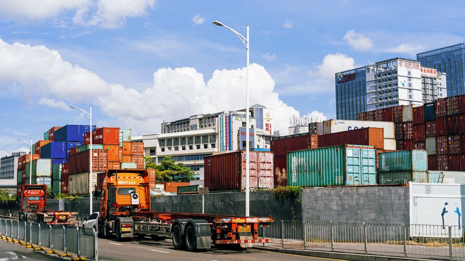 Stacked shipping containers at a harbor represent the freight and sourcing exposure facing home-furnishings companies.