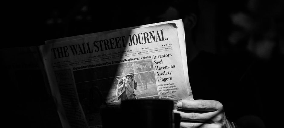A person reading a newspaper in monochrome, symbolizing financial news consumption.