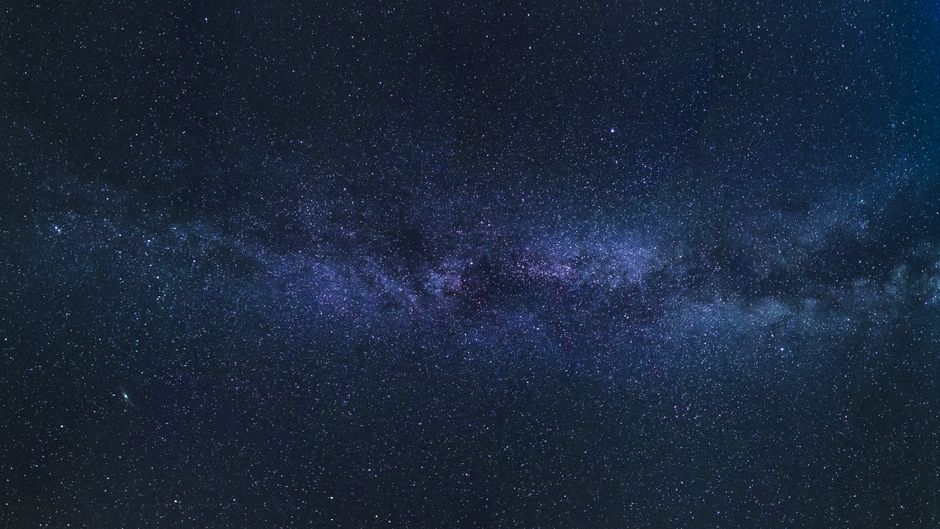 The Milky Way galaxy stretching across a dark night sky with countless stars in blue and purple hues.
