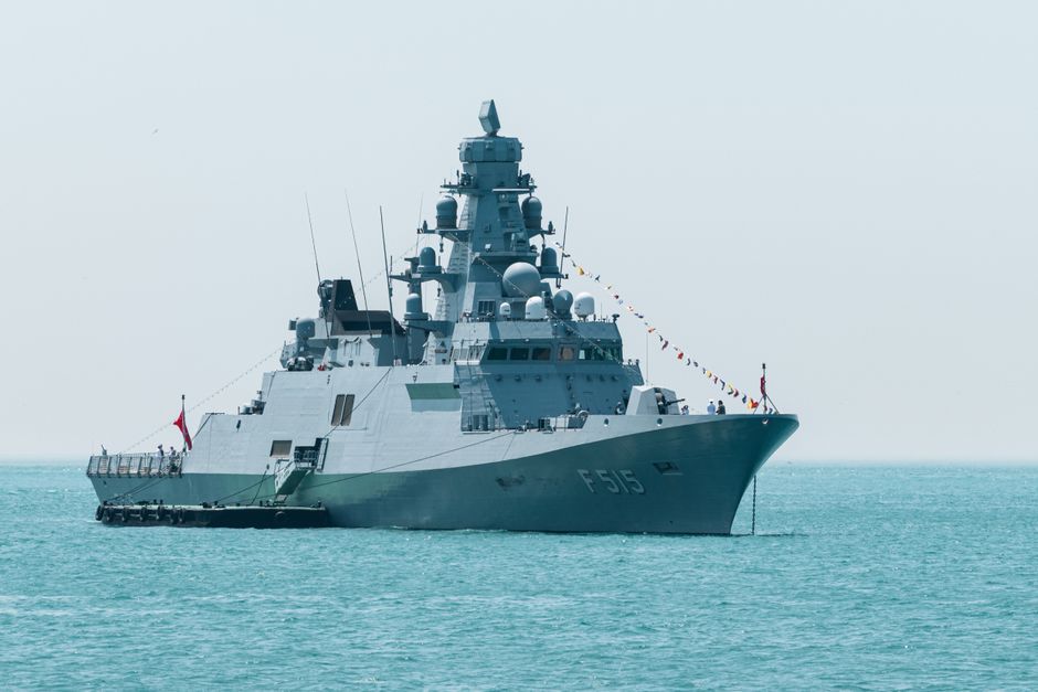 A naval warship with hull number F515 cruises on calm turquoise waters under a clear sky.