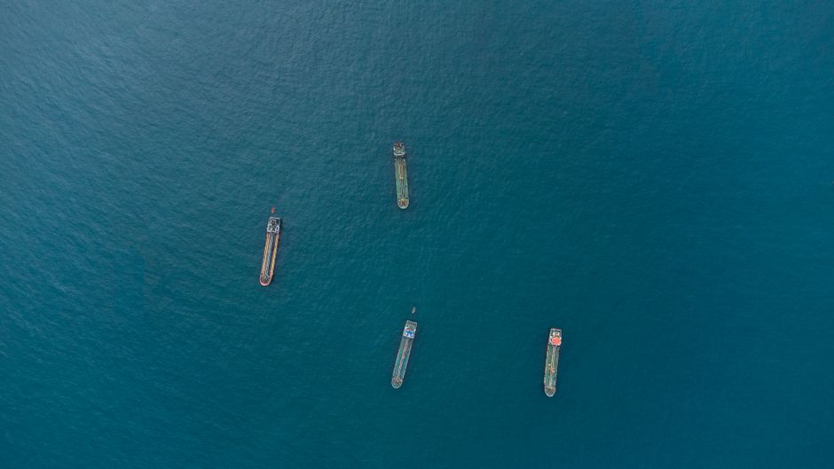 Aerial view of cargo ships traversing open ocean, illustrating the maritime shipping chokepoints at the center of the US-Iran conflict.