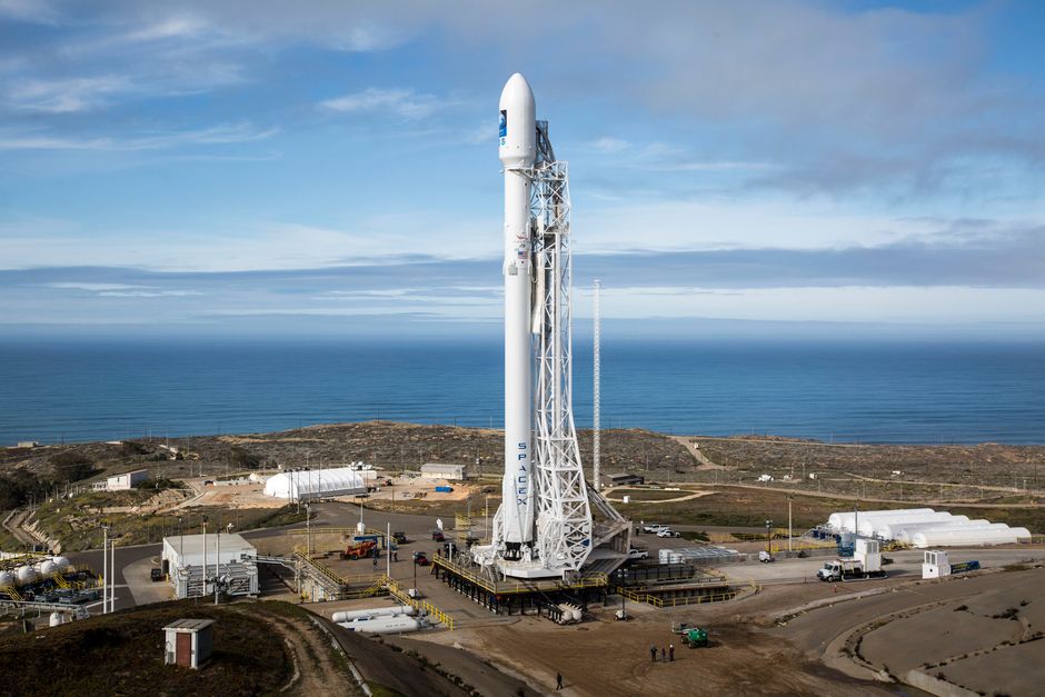 A SpaceX rocket stands on a launch pad overlooking the ocean under a clear sky.