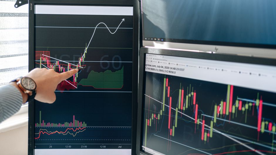 Stock market graphs displayed on dual monitors in a financial analysis workspace.