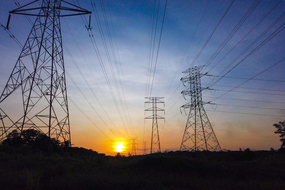 Silhouetted power transmission towers against a striking sunset sky, representing the energy infrastructure demand driven by AI data-center buildout.