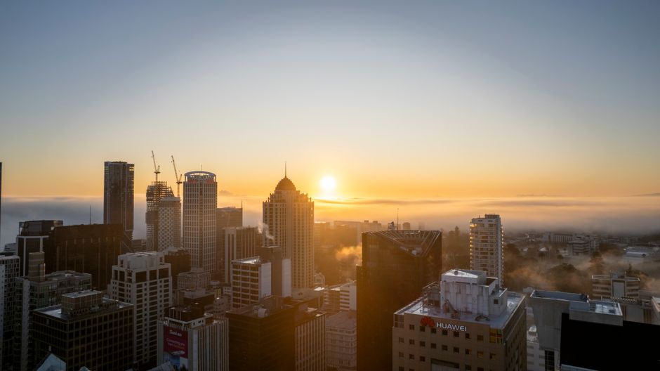 Aerial view of a modern city skyline at sunrise with fog partially obscuring skyscrapers, representing financial markets at the start of a trading day.