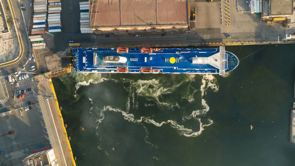 Aerial view of a large cargo ship docked at an industrial port with harbor infrastructure.