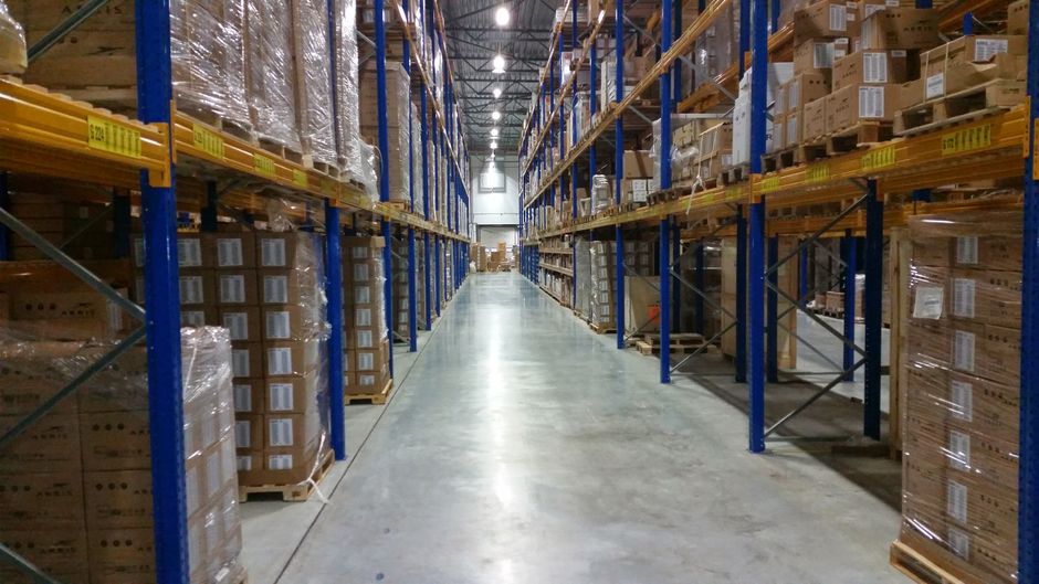 Interior of a large warehouse aisle lined with stacked cardboard boxes, representing Amazon's fulfillment and e-commerce operations