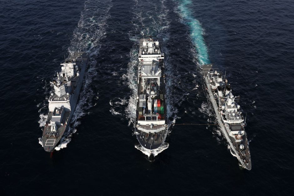 Naval warships sailing in formation on open sea, illustrating military protection of maritime chokepoints in the Middle East conflict zone.