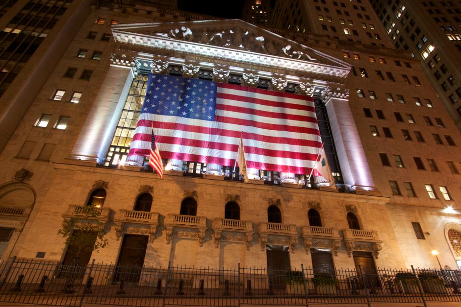 Nighttime view of the New York Stock Exchange building with an American flag illuminated on its facade