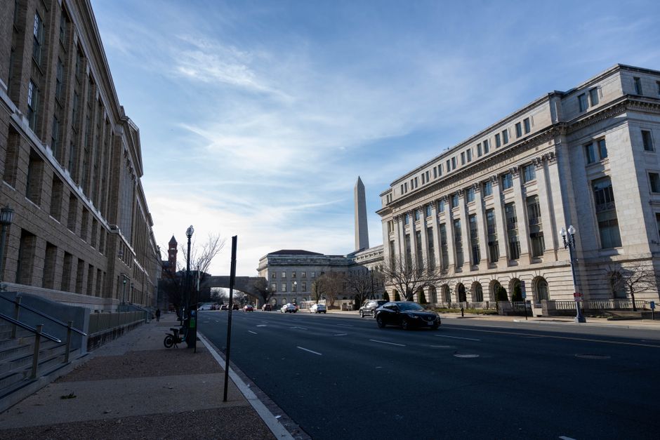 A Washington DC street with historic buildings and the Washington Monument in the distance.