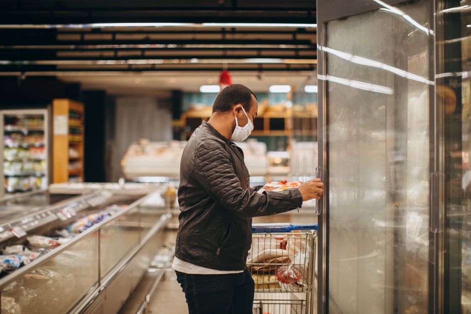 A shopper selecting items from a refrigerated section in a supermarket, representing the unexpected decline in July retail sales.