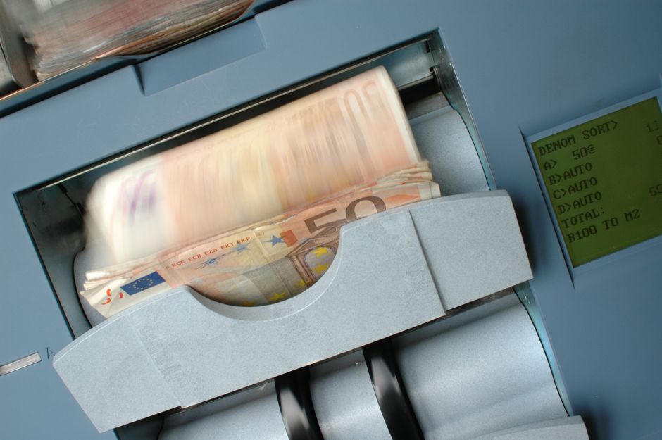 Currency moves through an automated counting machine, representing capital formation and the mechanics of liquidity.