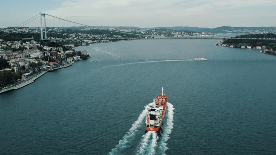 A cargo ship navigating a narrow international waterway, representing the maritime chokepoint at the center of the energy-supply risk.