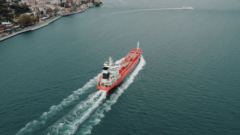 Aerial view of a large cargo ship navigating through a narrow maritime strait, symbolizing the critical chokepoint dynamics at the Strait of Hormuz