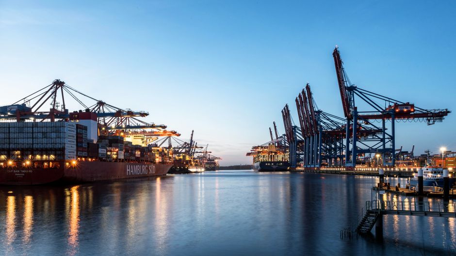 Illuminated cargo ships and cranes at a port at dusk, highlighting global shipping and maritime logistics.
