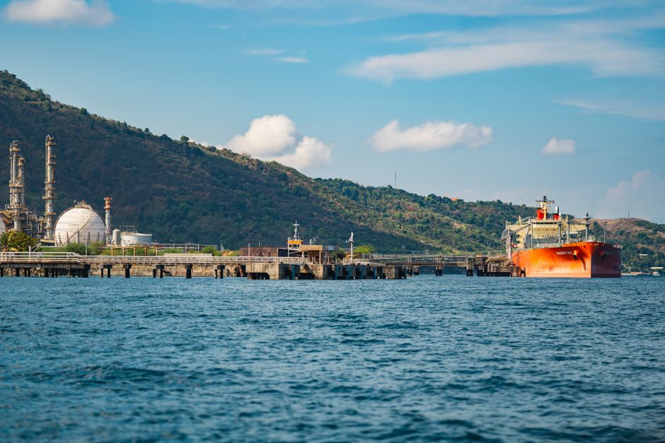 An oil tanker at an industrial port represents the next transmission point from shipping disruption to the real economy