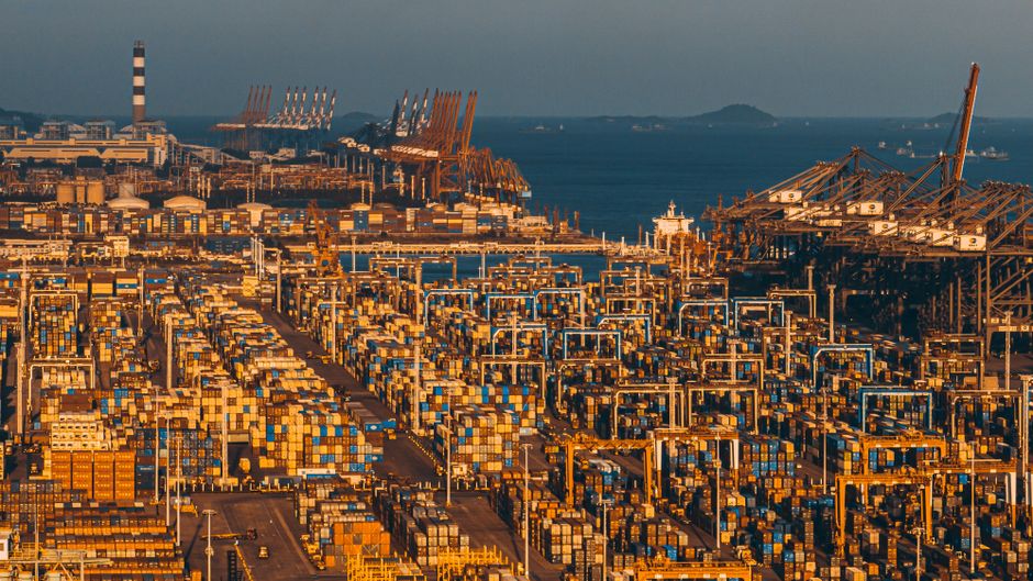 Aerial view of cargo containers at a busy commercial port as geopolitical risk raises logistics costs.