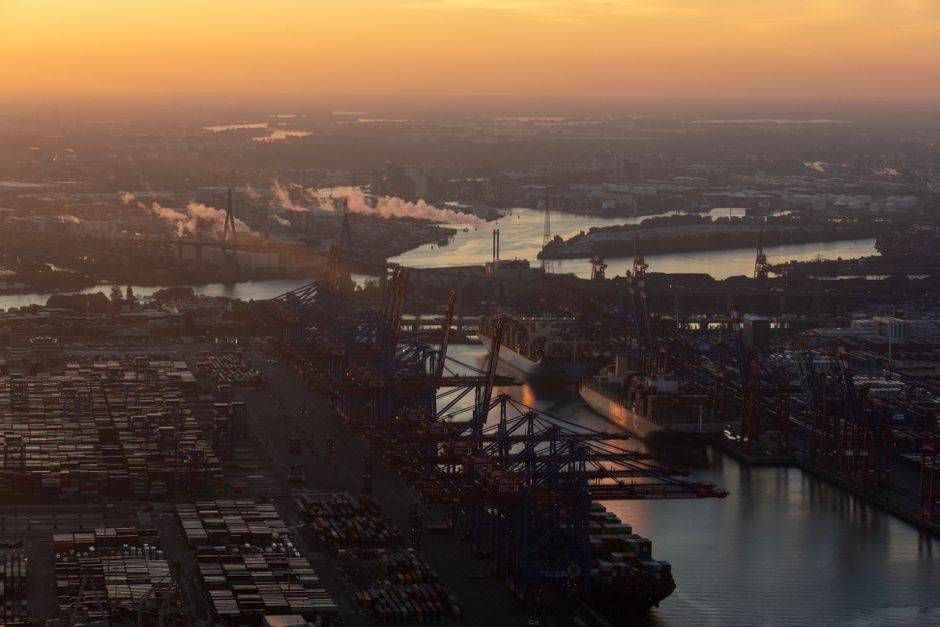 Aerial view of a bustling port at sunrise with cranes and container ships, representing critical global shipping infrastructure.