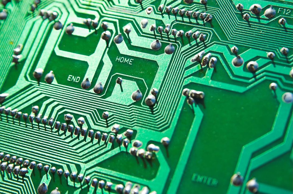 A green circuit board with visible chips and electronic pathways, representing semiconductor technology.