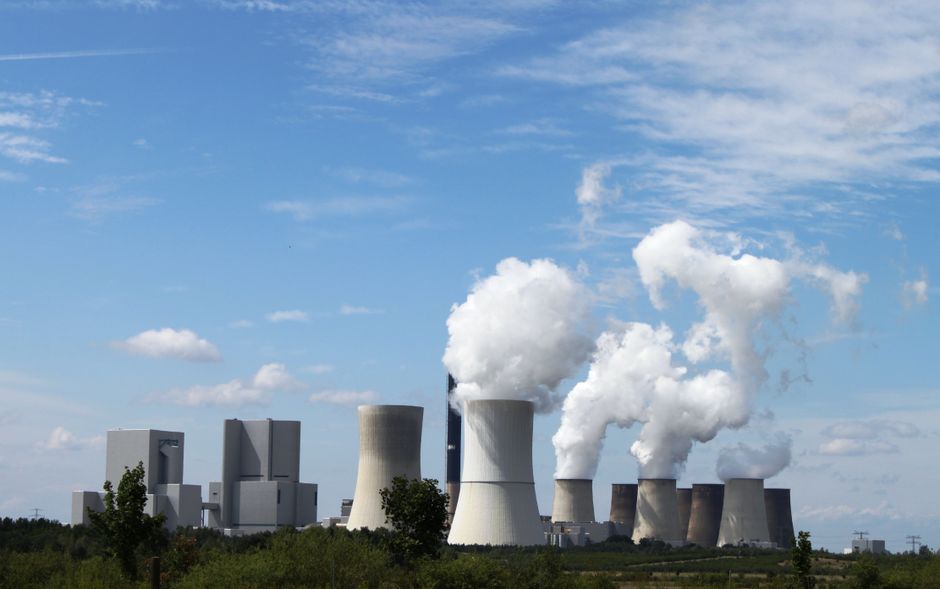 Wide view of a power station with chimneys releasing steam under a clear blue sky
