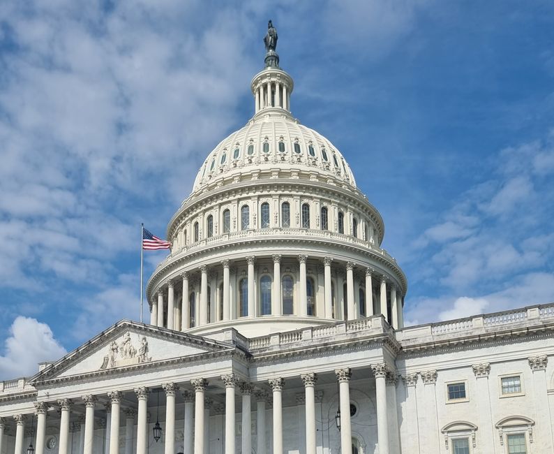 The US Capitol dome with flag against a blue sky