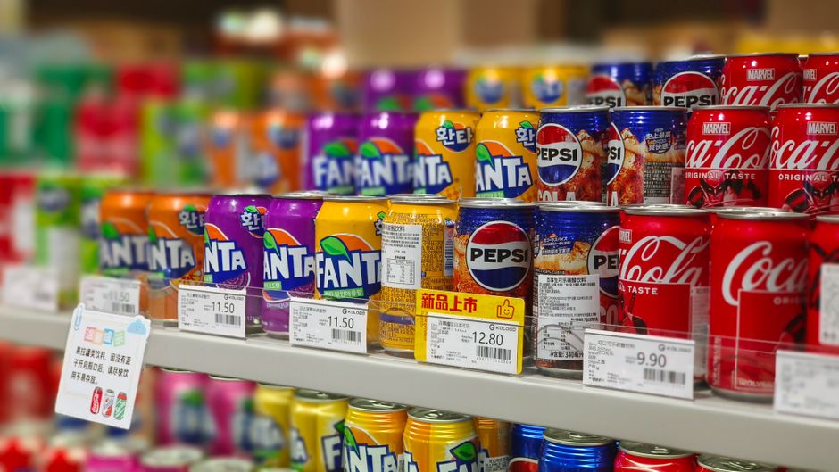 Supermarket shelves lined with colorful beverage cans and visible price tags.
