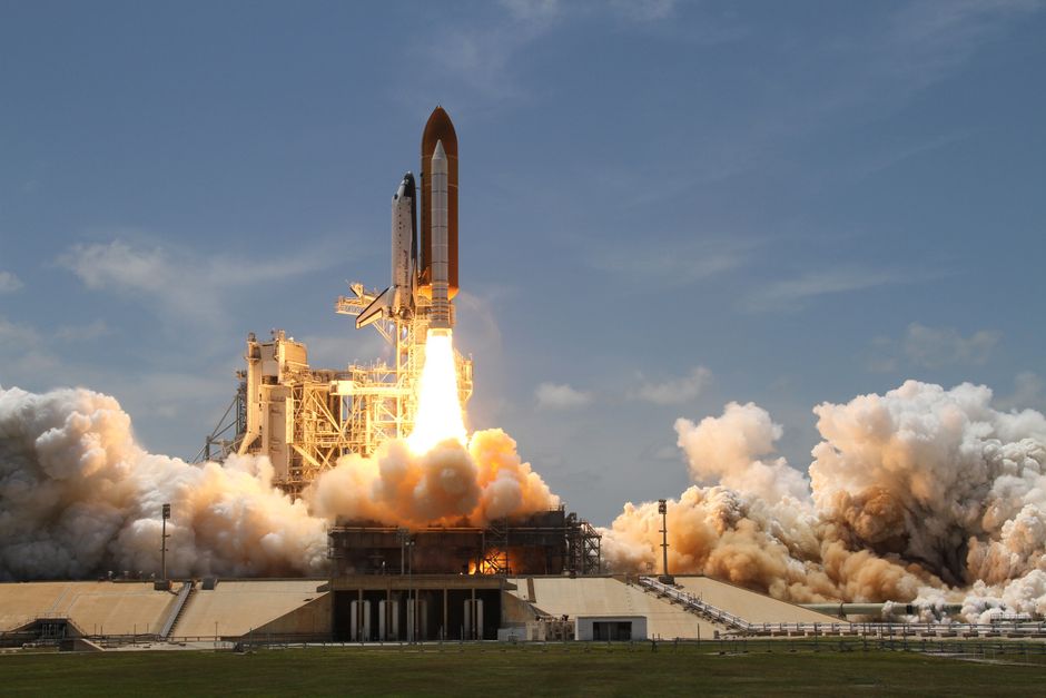 A space shuttle launches with fiery liftoff, ascending into the sky amid plumes of smoke