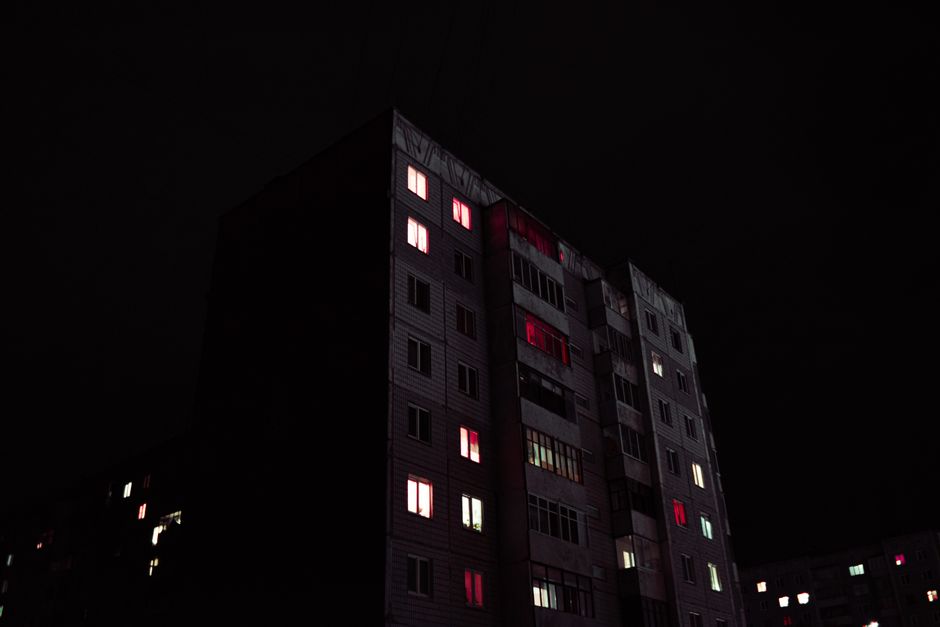 A tall building with illuminated windows stands against a dark night sky, creating a mysterious urban atmosphere.