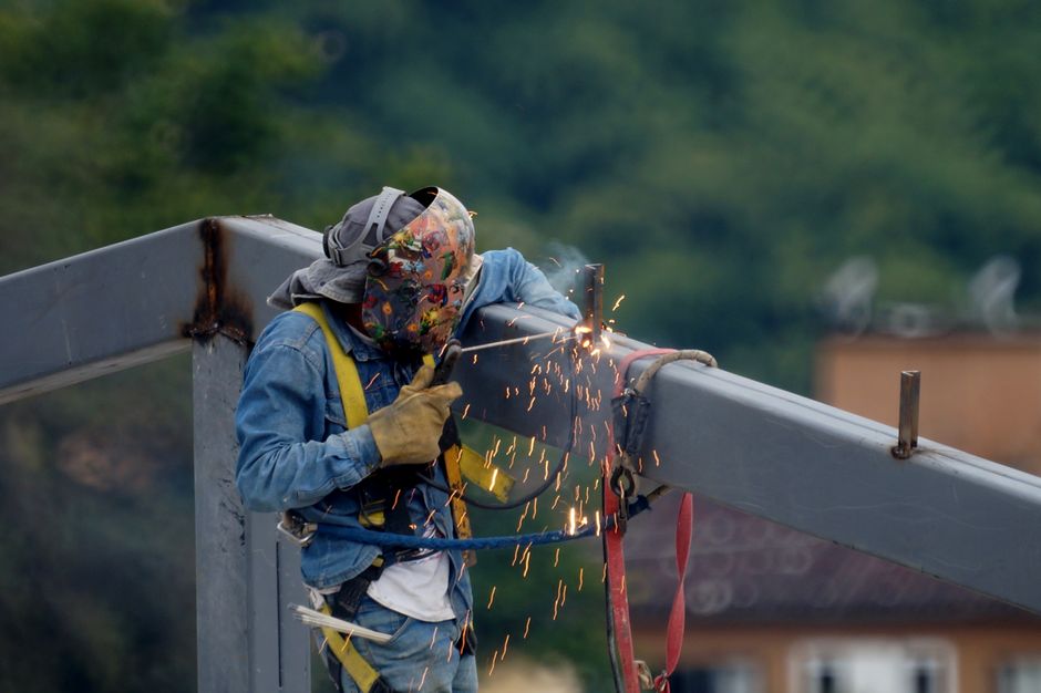 A construction worker welding a steel beam outdoors, representing the labor market that surprised markets with an unexpected payroll decline.