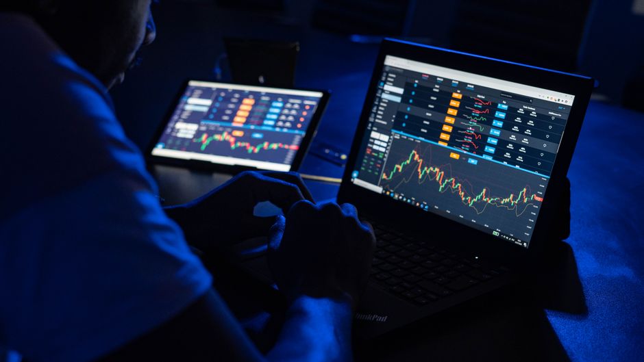 Trader reviewing multiple market charts on laptop screens in a dark workspace