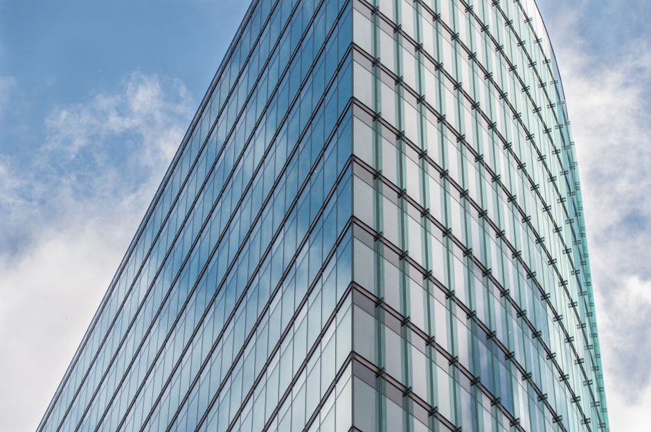 Modern glass skyscraper reflecting blue sky and clouds in a financial district.