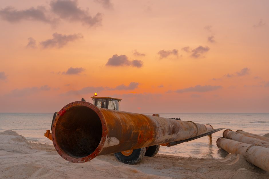 Heavy machinery moving large steel pipes at a construction site