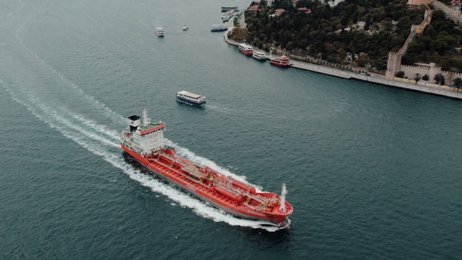 Aerial view of a large cargo ship navigating through a narrow strait under cloudy skies, illustrating maritime oil transit chokepoints.