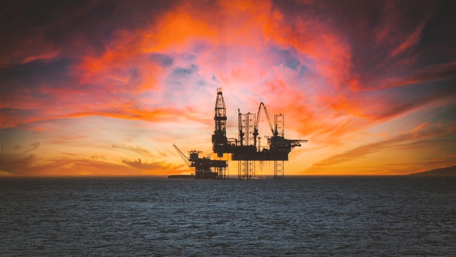 An offshore oil drilling platform silhouetted against a sunset, representing the energy markets roiled by the Iran conflict de-escalation.
